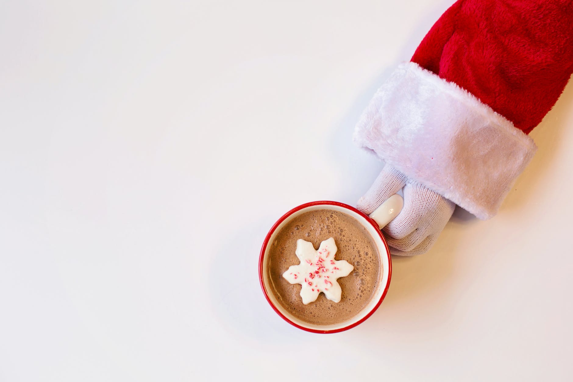 mug of chocolate drink with snowflake shaped cookie on top held by a person in santa suit