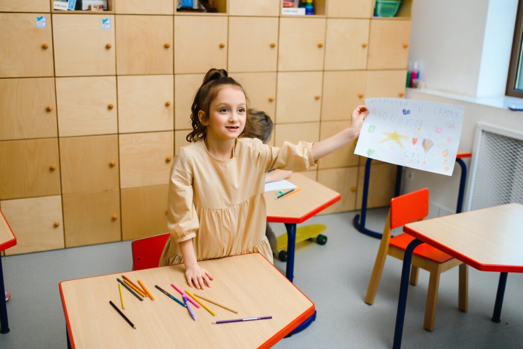 Girl in classroom holding up one of her drawings