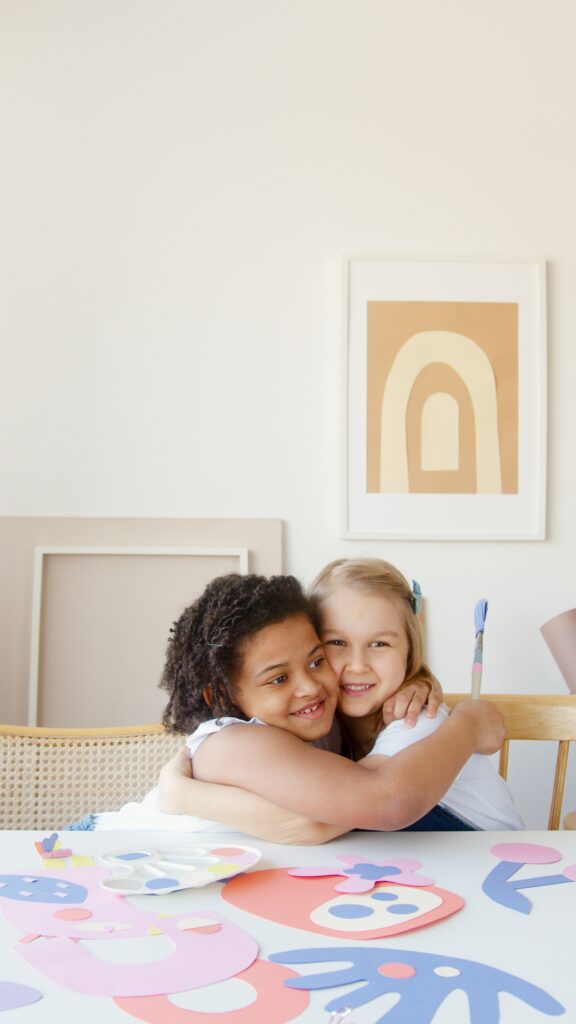 Picture of two girls hugging with their art work laid out on the table.