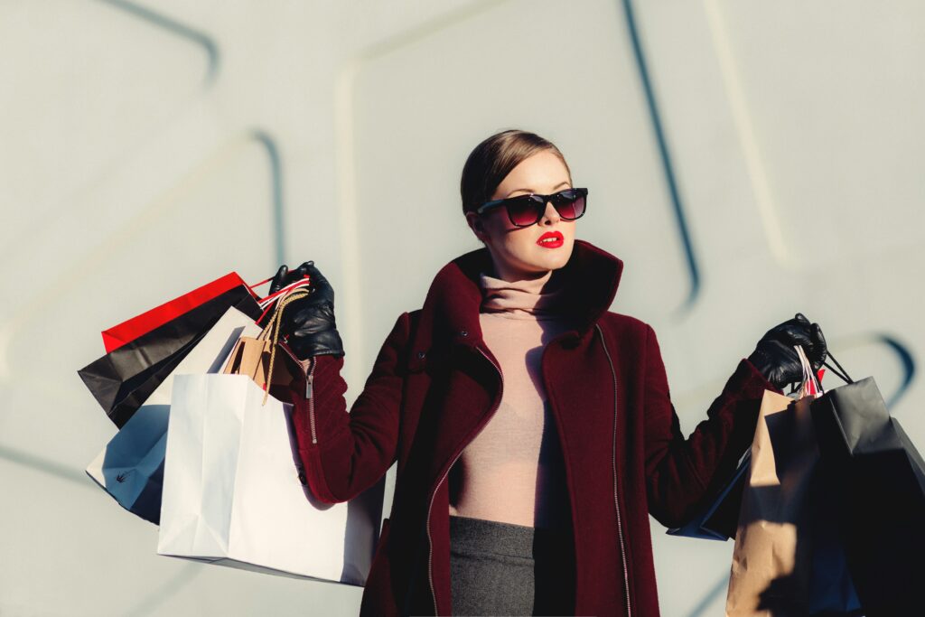 Woman with sunglasses carrying multiple shopping bags in each handd.