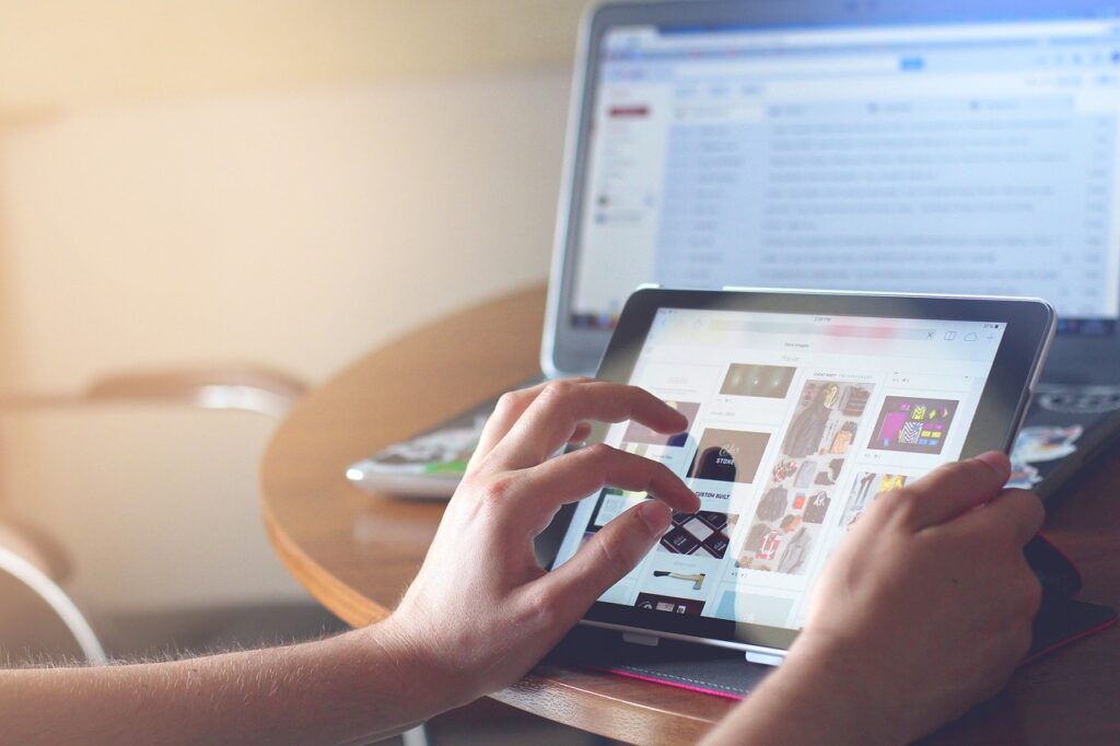 Person sitting in front of a laptop, playing with her tablet 