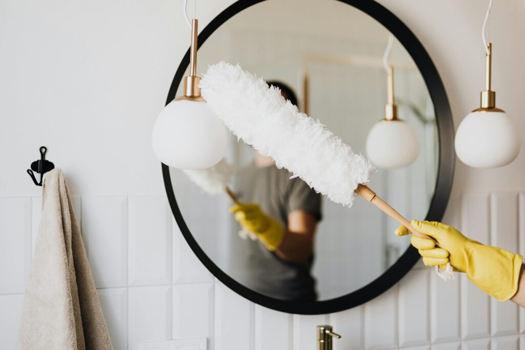 Person in front of a mirror with a feather duster wearing yellow gloves 