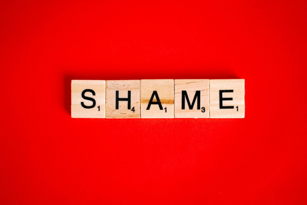 The word Shame laid out in Scrabble blogs on a red background
