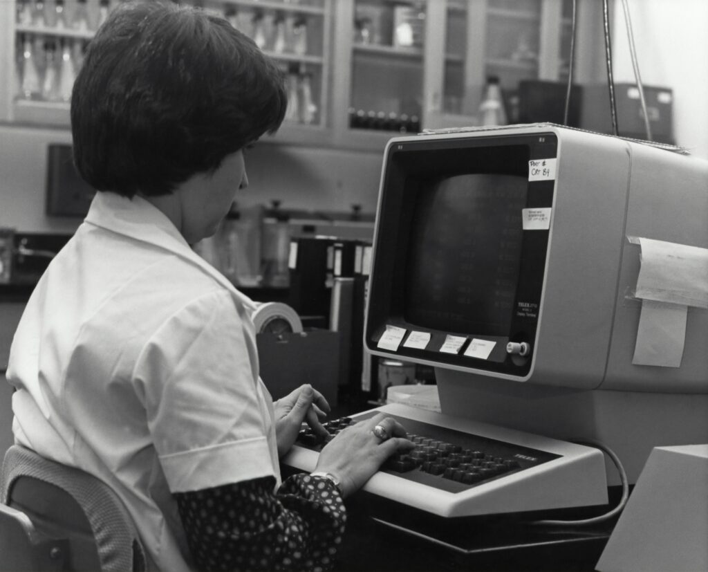 Woman in lapcoat working on a PC, early 80s.