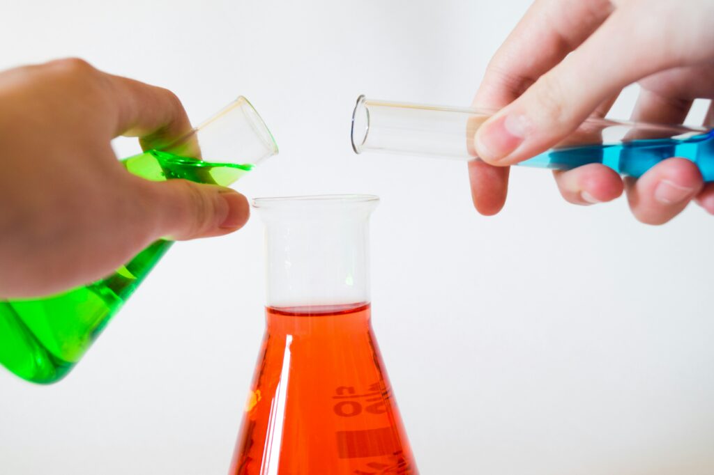 Two hands decanting liquid into test tubes.